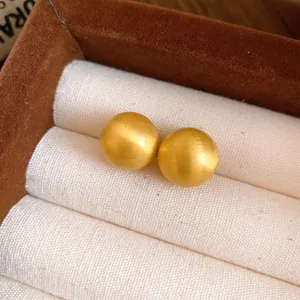 Close-up of golden spherical stud earrings with brushed matte finish in jewelry box