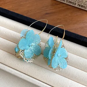 Close-up of blue fabric flower earrings with elegant gold-toned hollow petal design