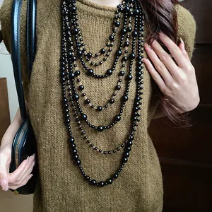Close-up of multi-layer black acrylic bead necklace styled with a green knit sweater