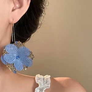 Detail shot of a blue textured flower ear hook with gold filigree and rhinestone