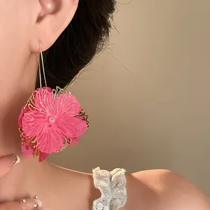 Close-up of large pink fabric flower earrings with gold hollow frame worn on a model's ear