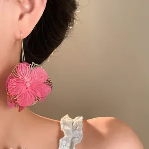Close-up of large pink fabric flower drop earrings with gold hollow detail on a model