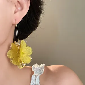 Close-up view of elegant oversized yellow mesh flower drop earrings worn by a model