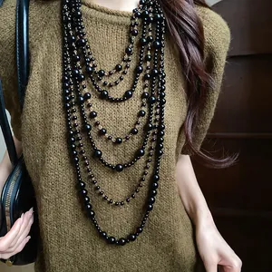 Detailed view of a multi-layered black acrylic bead long necklace on a knit sweater.
