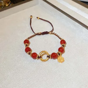 Detailansicht eines handgefertigten Armbands mit roten Perlen und goldenen Anhängern.