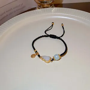 Detailaufnahme eines handgeflochtenen Armbands mit goldenem Jade-Anhänger