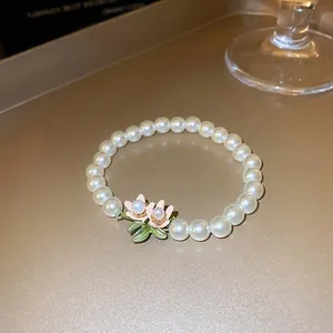 Makro-Detail eines handgefertigten Perlenarmbands mit elegantem rosa Lotusblumen-Anhänger.