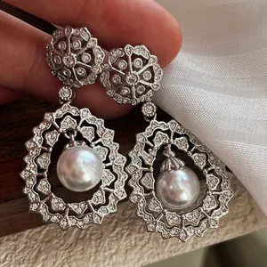 Close-up of sparkling silver-toned earrings with intricate crystal pavé and large central pearls