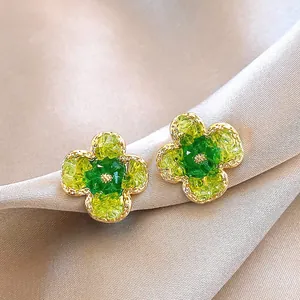 Elegante goldfarbene Blumen-Ohrstecker mit grünen und gelben Kristallen in der Nahaufnahme.