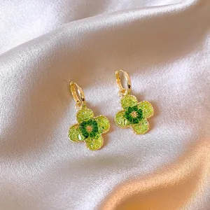 Detailansicht goldener Blumenohrringe mit grünen Kristallen auf weichem Seidenhintergrund
