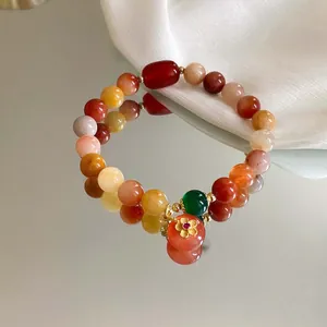 Detailansicht eines bunten Perlenarmbands mit goldenem Blumenanhänger auf einem Spiegel.