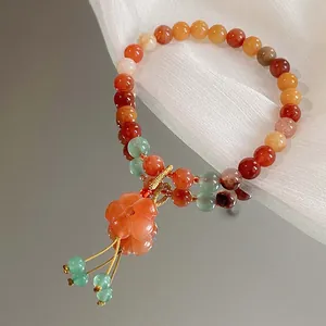 Nahaufnahme eines handgefertigten Perlenarmbands mit orangefarbener Blüte und Quasten