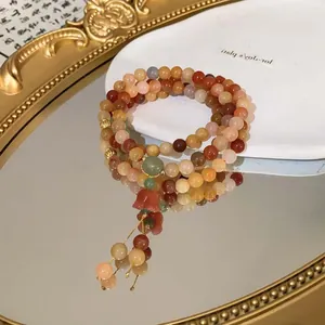Detail des mehrreihigen Perlenarmbands mit rotem Blumenanhänger und Quasten