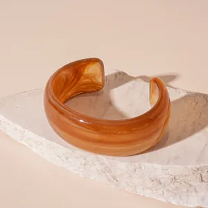 Macro detail of amber-patterned acrylic cuff bangle on white stone pedestal.