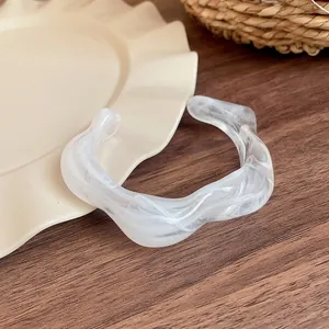 Detailed view of a white marbled acrylic bangle with an irregular wavy design on wood.