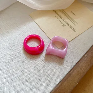 Close-up detail of minimalist pink resin geometric rings on a textured linen background