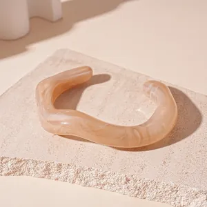 Close-up detail of beige acrylic wavy cuff bracelet with elegant marbled texture