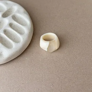 Close-up detail of a minimalist ivory-white geometric resin ring on a beige background