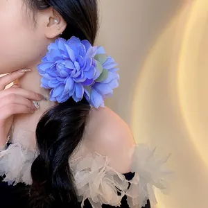 Dettaglio di un grande fermaglio per capelli a fiore in tessuto blu su capelli scuri mossi.