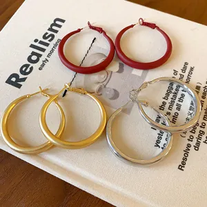 Close-up of minimalist S925 silver needle hoop earrings in red, gold, and silver on a book.
