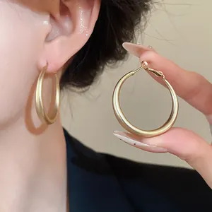 Detailed macro view of a minimalist matte gold hoop earring held by hand to show texture
