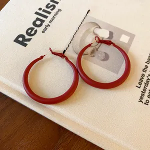Close-up detail of matte red minimalist circular hoop earrings on a textured background