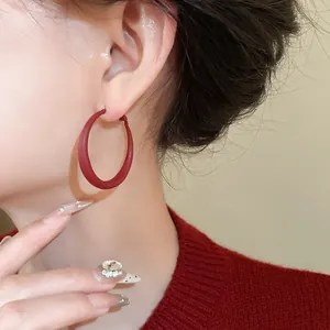 Close-up view of minimalist red matte hoop earrings worn by a model in a red sweater.