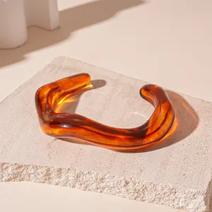 Close-up detail of an irregular wavy amber acrylic cuff bracelet with marble texture