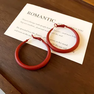 Detailed macro view of matte red geometric hoop earrings on a vintage wooden tray.