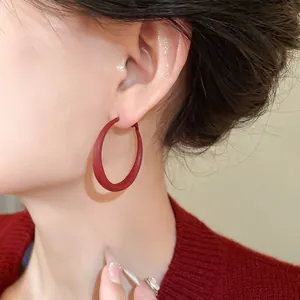 Close-up view of minimalist red geometric hoop earrings worn by a model in a red sweater