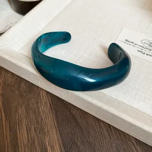 Close-up detail of a marbled teal acrylic bangle featuring an irregular wavy design