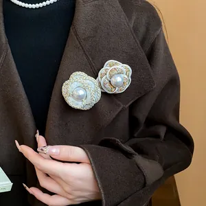 Detail view of elegant French camellia brooches with pearls on a brown wool coat