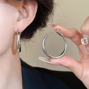 Detailed view of minimalist thick silver hoop earrings being worn and held by a hand