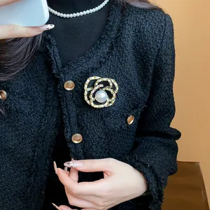 Detail of a vintage French-style gold camellia brooch with a central pearl on a tweed jacket.
