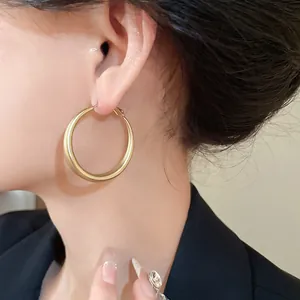 Close-up of a model wearing large gold-tone geometric hoop earrings with matte finish.