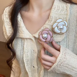 Close-up detail of elegant camellia brooches with pearls and gold chains on a cardigan.