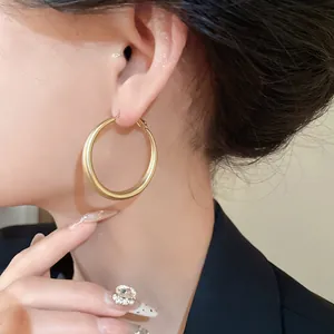 Detail of gold-finished chunky hoop earrings with silver needle on model ear