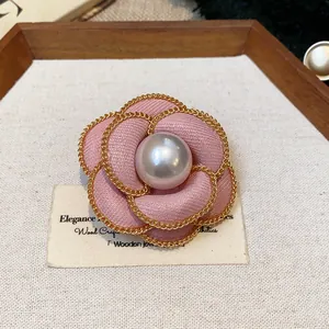 Detailed macro view of pink fabric camellia brooch with gold chain and pearl center