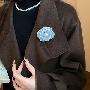 Detailed macro view of an elegant blue fabric camellia brooch with pearl on a brown coat.