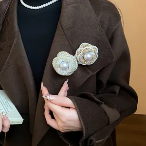 Close-up of elegant camellia brooches with pearl center on a brown wool coat