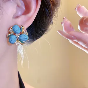 Dettaglio ravvicinato di eleganti orecchini vintage con turchese blu e zirconi sul lobo.