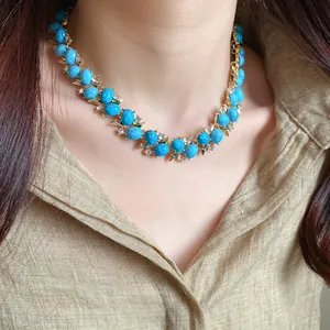 Primo piano di una collana vintage con turchese e zircone abbinata a una camicia di lino