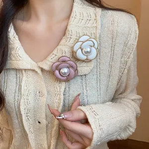 Close-up of elegant camellia brooches with pearls on a cream knit cardigan.