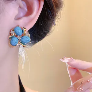 Primo piano di orecchini vintage in resina turchese e zirconi su modella elegante.