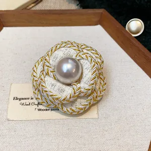 Close-up detail of a French-style camellia brooch with woven gold trim and a central pearl
