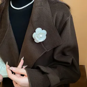 Close-up detail of an elegant white camellia brooch with central pearl on brown coat