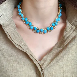 Primo piano di una collana vintage in resina turchese e zirconi su una camicia di lino.