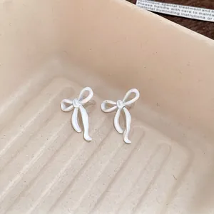 Dettaglio macro di eleganti orecchini a lobo a fiocco bianco laccato con perni in argento