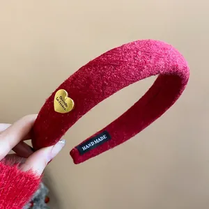 Close-up of red textured wide headband with gold heart charm and handmade label.