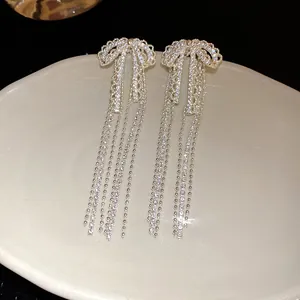 Macro view of glittering zircon bow earrings with delicate tassels on an ivory display plate